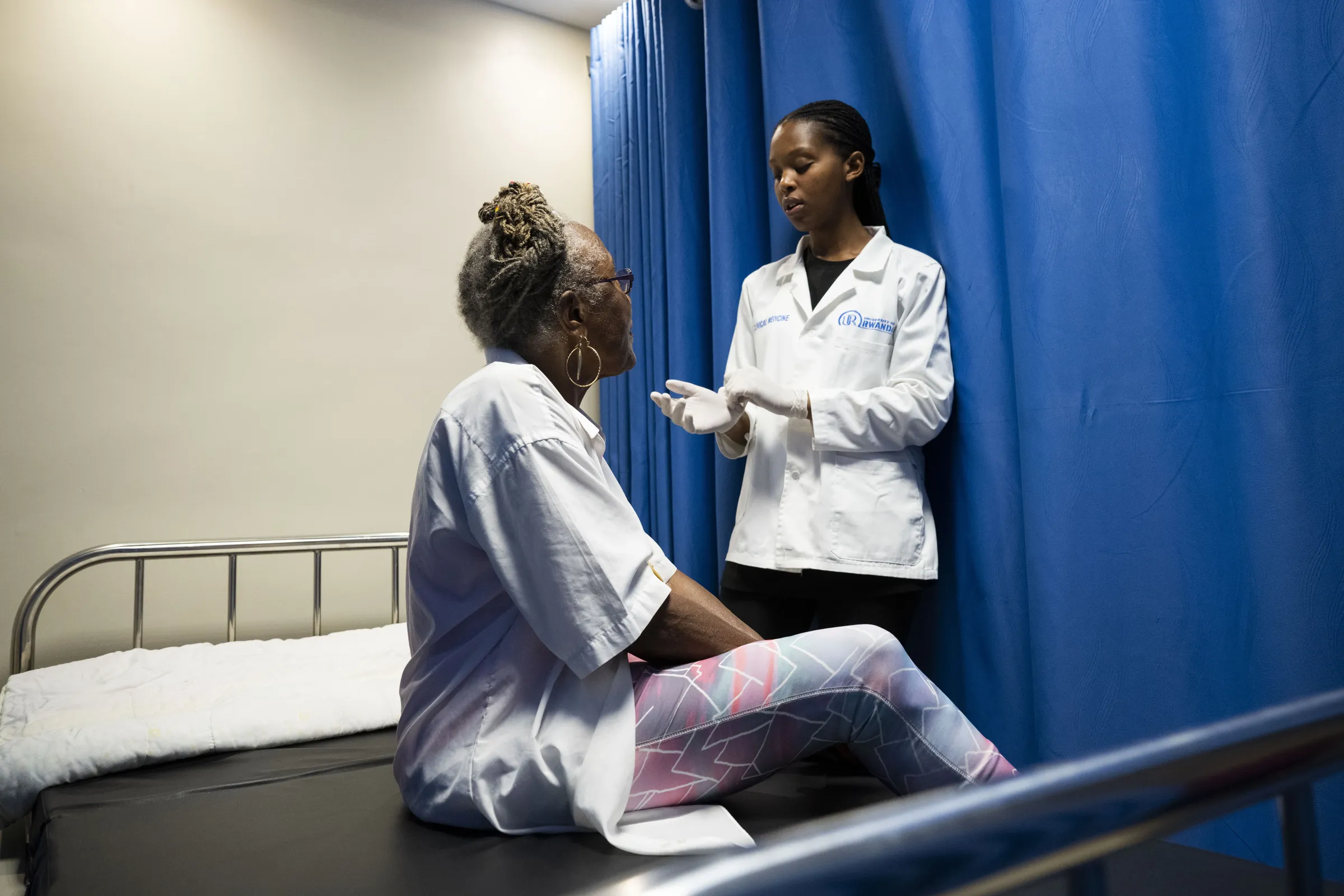 A healthcare professional speaking privately with a seated woman in a clinical examination room